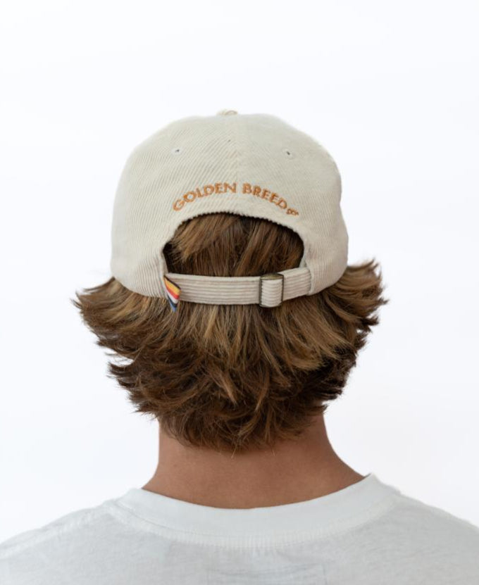 Person with medium-length brown hair wearing the Golden Breed Hancock Cord Cap in off white, featuring GOLDEN BREED embroidery on the back, viewed from behind against a plain white background.