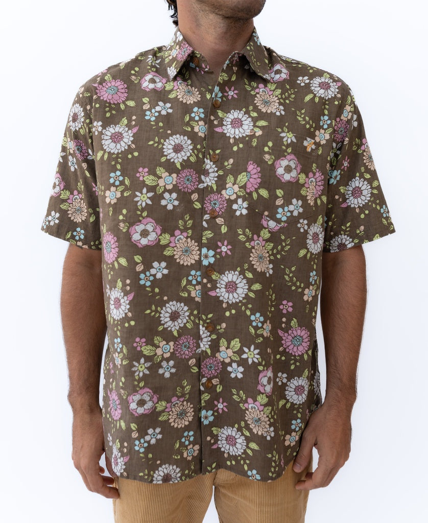 A man wearing the Golden Breed Happy Floral Shirt in Wash Brown, a short-sleeve button-up with a pink, white, and green floral pattern.