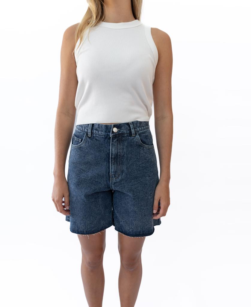 A woman stands against a plain white background wearing a sleeveless white top and Golden Breeds Izzy Short in Dark Blue.