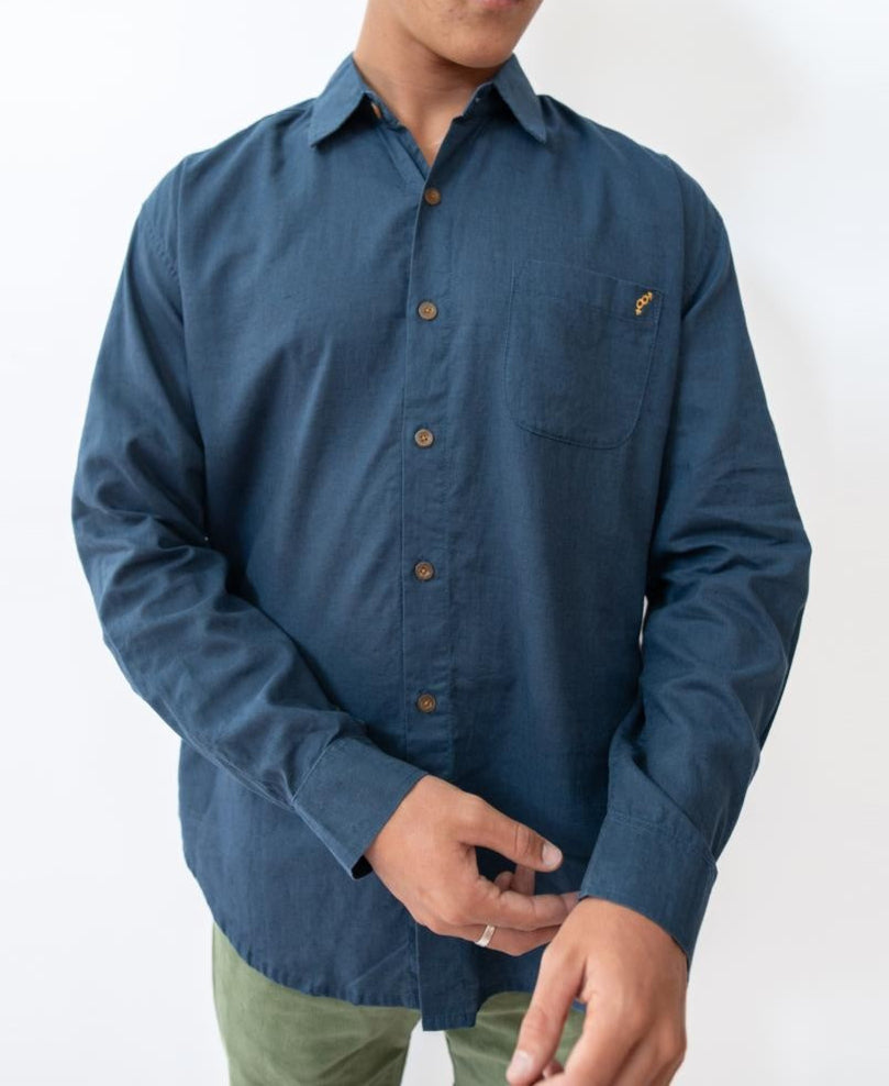 A person wears the Golden Breed Linen LS Shirt in Vintage Navy with a chest pocket and green pants, standing against a plain white background.