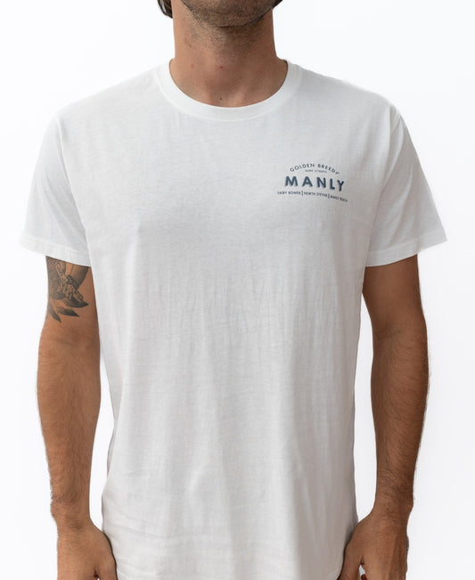 A person wearing the Golden Breed Manly Old School Tee | Off White, a 100% cotton shirt with a small Manly logo and text on the upper left chest, stands against a white background.