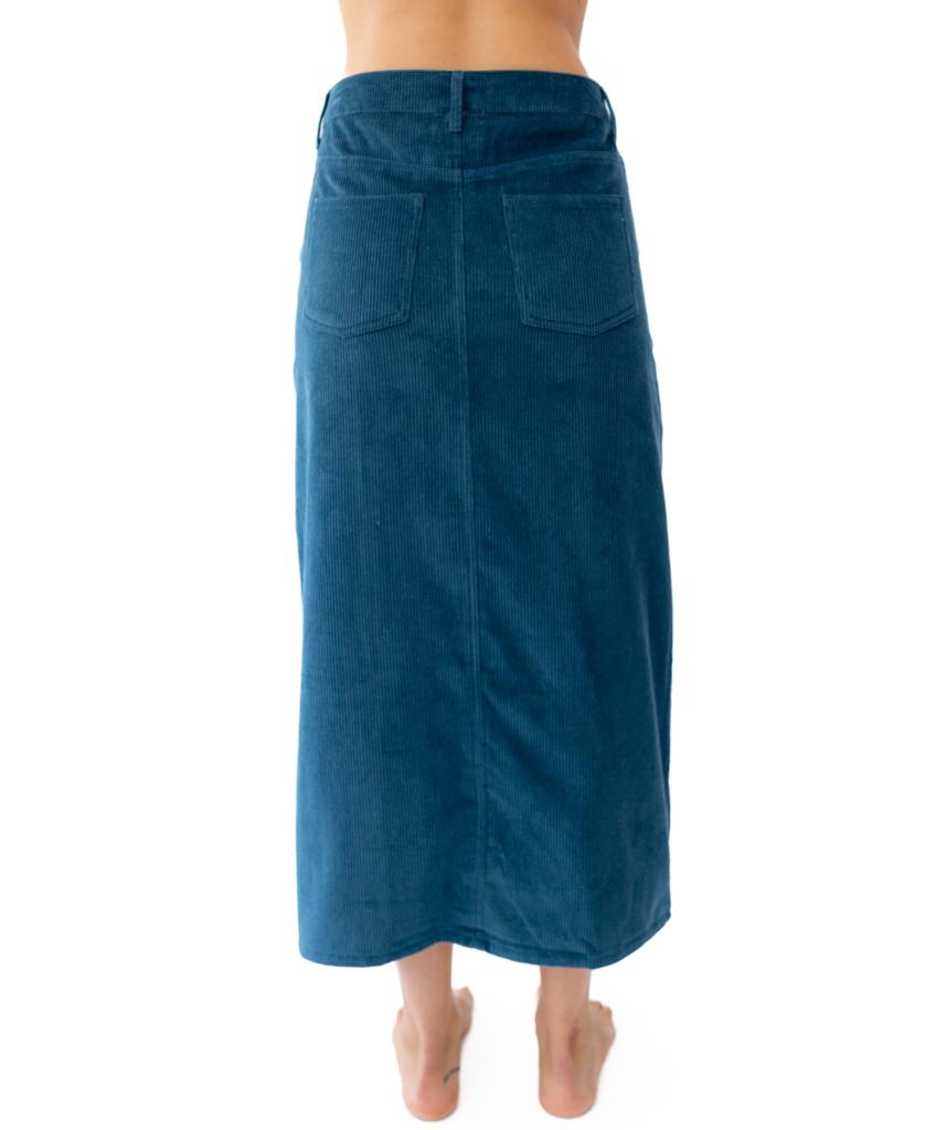 A person stands barefoot in a blue Nellie Maxi Skirt | Petrol by Golden Breed, shown from the back against a white background.