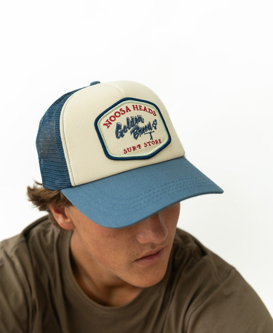 A person wearing the Golden Breed Noosa Trucker Cap | Dark Denim with a NOOSA HEADS patch, paired with dark denim, looking slightly downward.