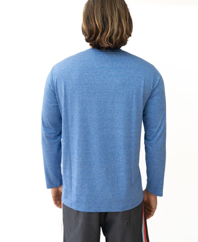 A person with shoulder-length hair, wearing the Golden Breed Pebbles L/S Rash Shirt in Blue Marle (UPF 50+) and dark shorts, stands with their back to the camera against a white background.