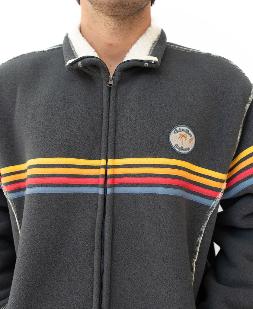 A person wearing the Golden Breed Reef Bonded Sherpa Jacket in Wash Black, featuring red, yellow, and orange chest stripes and a circular “California Clubland” patch.