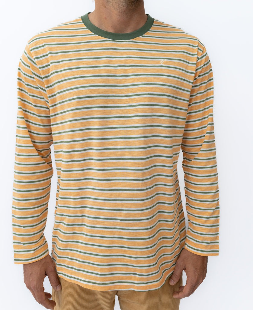 A person wears the Golden Breed Rincon Stripe LS Tee in Wash Orange, featuring orange, green, and white stripes with a green collar, paired with light brown pants against a plain white background.