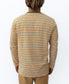 Someone stands facing away, wearing the Golden Breed Rincon Stripe LS Tee | Wash Orange—crafted from soft cotton jersey with orange, white, and green stripes—paired with tan pants.