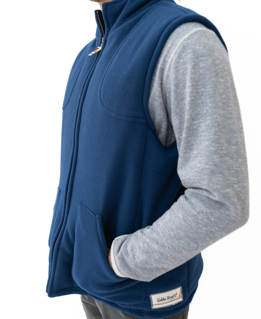A person in a midnight Thredbo Vest by Golden Breed, crafted from polyester polar fleece, layered over a gray long-sleeve shirt with hands in the vest pockets, photographed from the side.