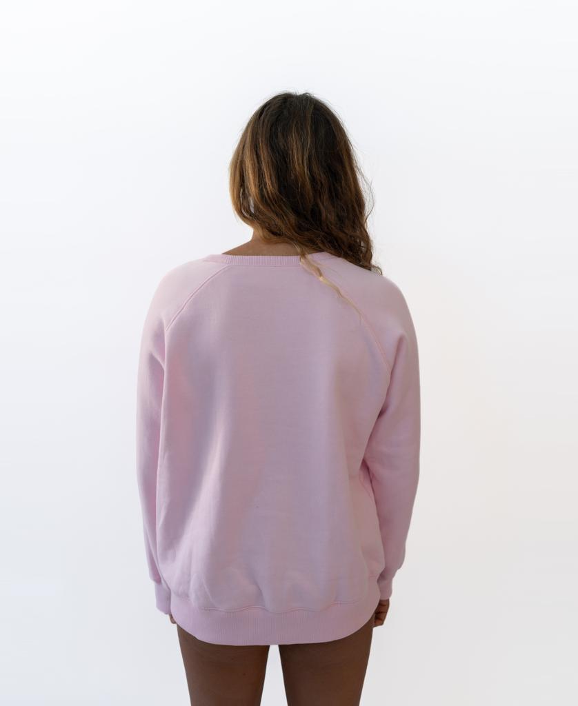 A person with long brown hair faces away from the camera, wearing the Vintage Sweat | Pale Pink sweatshirt by Golden Breed in 100% cotton fleece, featuring a retro logo, set against a plain white background.