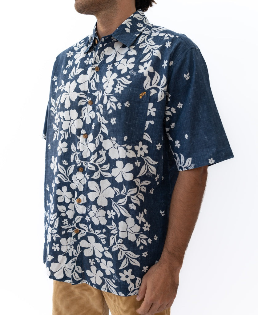A person wearing the Golden Breed Vomo Floral Shirt in vintage navy, featuring a white floral print, paired with light brown linen pants and standing against a white background.