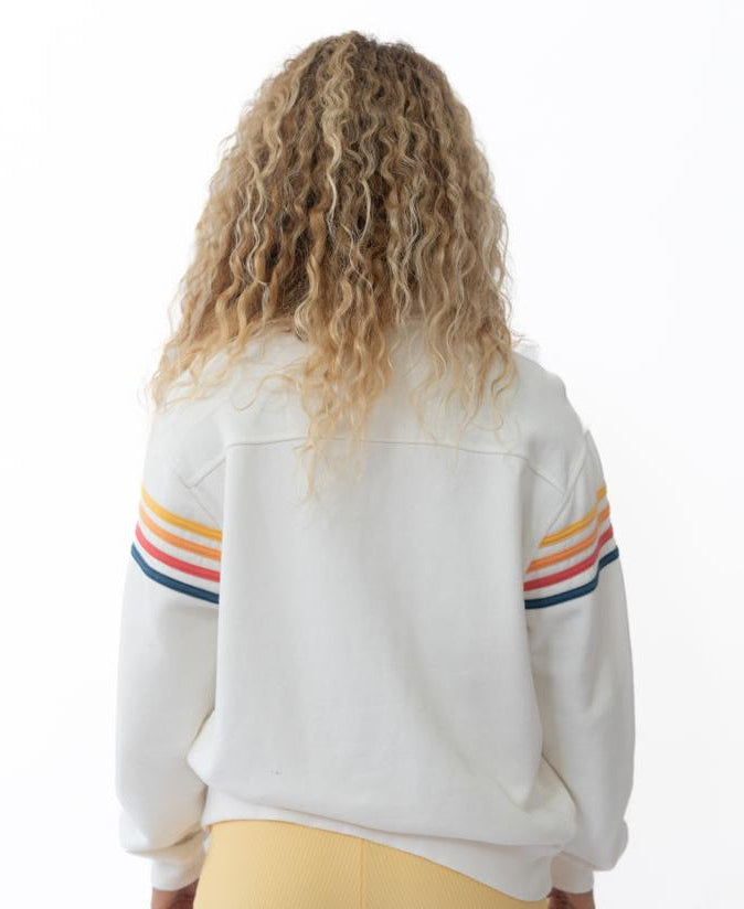 A person with curly hair wears the Golden Breed Long Island 1/4 Zip in Off White, featuring colorful sleeve stripes and yellow shorts, standing with their back to the camera against a white background.