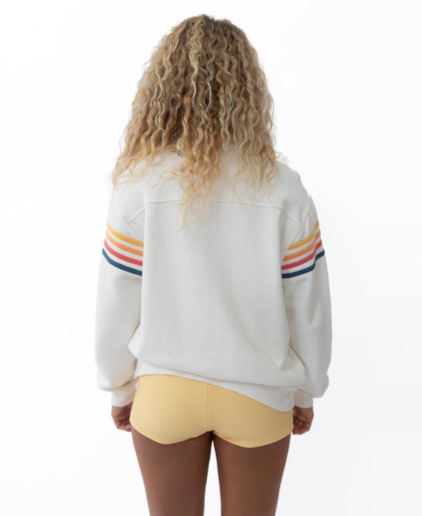 A person with curly hair wears the Golden Breed Long Island 1/4 Zip in Off White, featuring colorful sleeve stripes and yellow shorts, standing with their back to the camera against a white background.