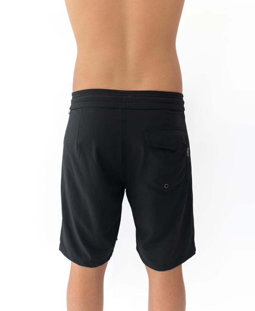 A person is shown from the back against a plain white background, wearing black G&S Boardie shorts by Gordon & Smith, made from recycled polyester.