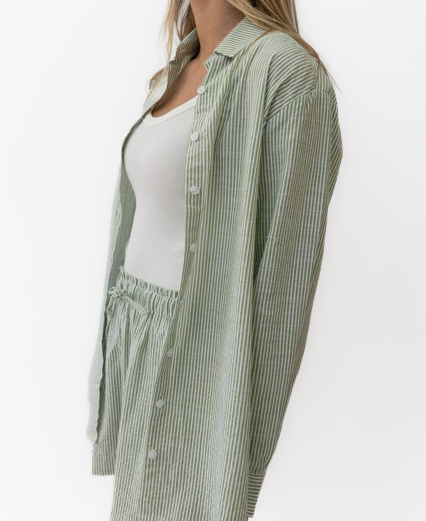 A person wears the Lazy Beach Maeve L/S Shirt in Olive Stripe with matching shorts over a white ribbed tank top, posed against a plain white background.