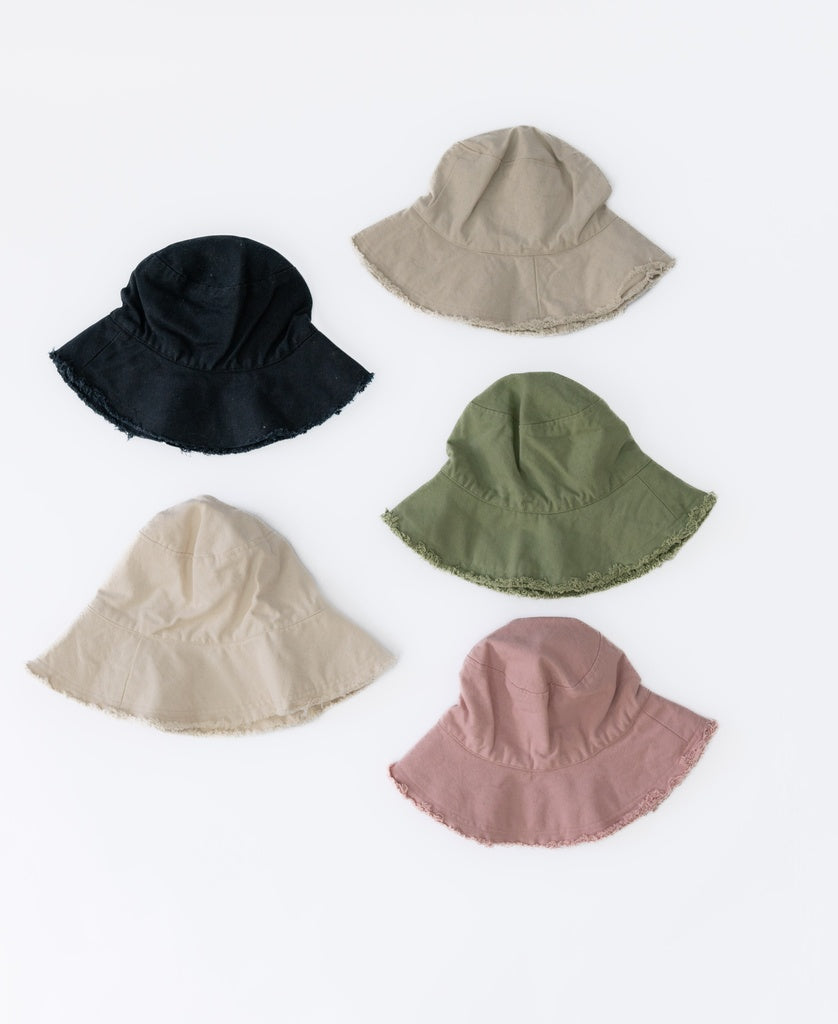 Five Lazy Beach Halo Bucket Hats in black, beige, green, cream, and pink are arranged on a white background, each featuring frayed edges.
