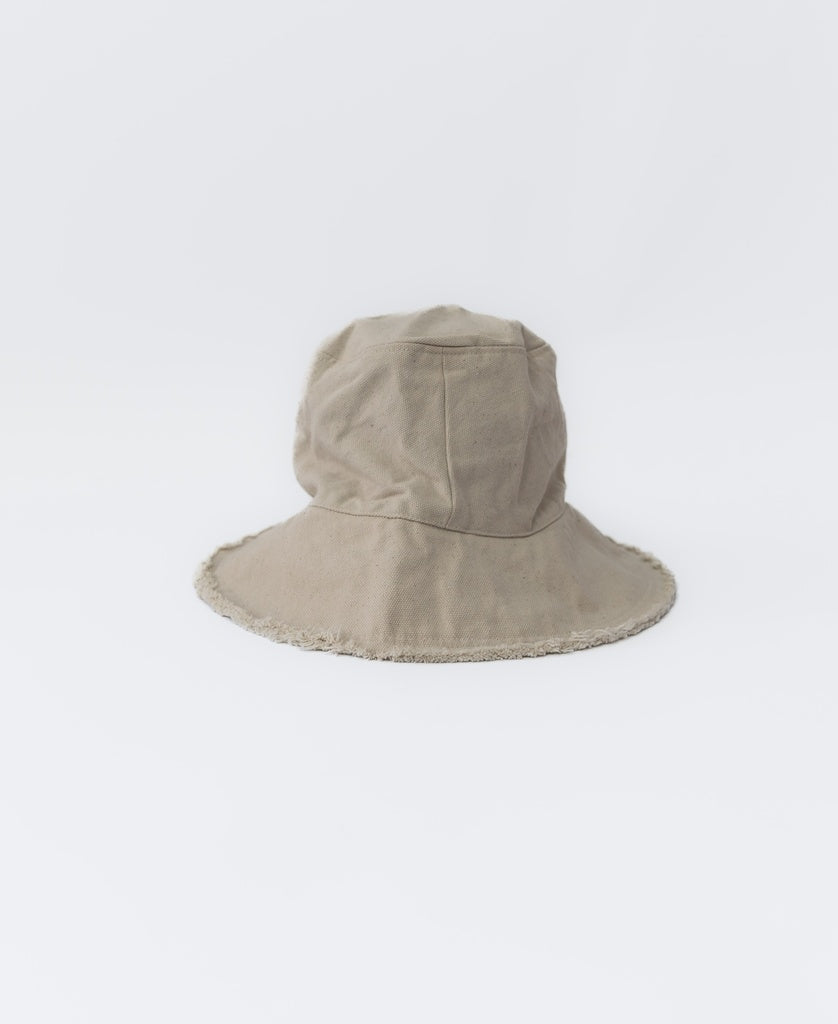 The Lazy Beach Halo Bucket Hat | Natural is a beige, wide-brimmed fabric hat with a slightly floppy shape, handmade in Indonesia. Shown against a plain white background, its perfect for stylish sun protection.