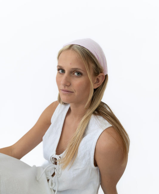A woman with long blonde hair wears the Lazy Beach Head Scarf in Pink Stripe, handmade in Bali, paired with a white sleeveless top against a plain white background.