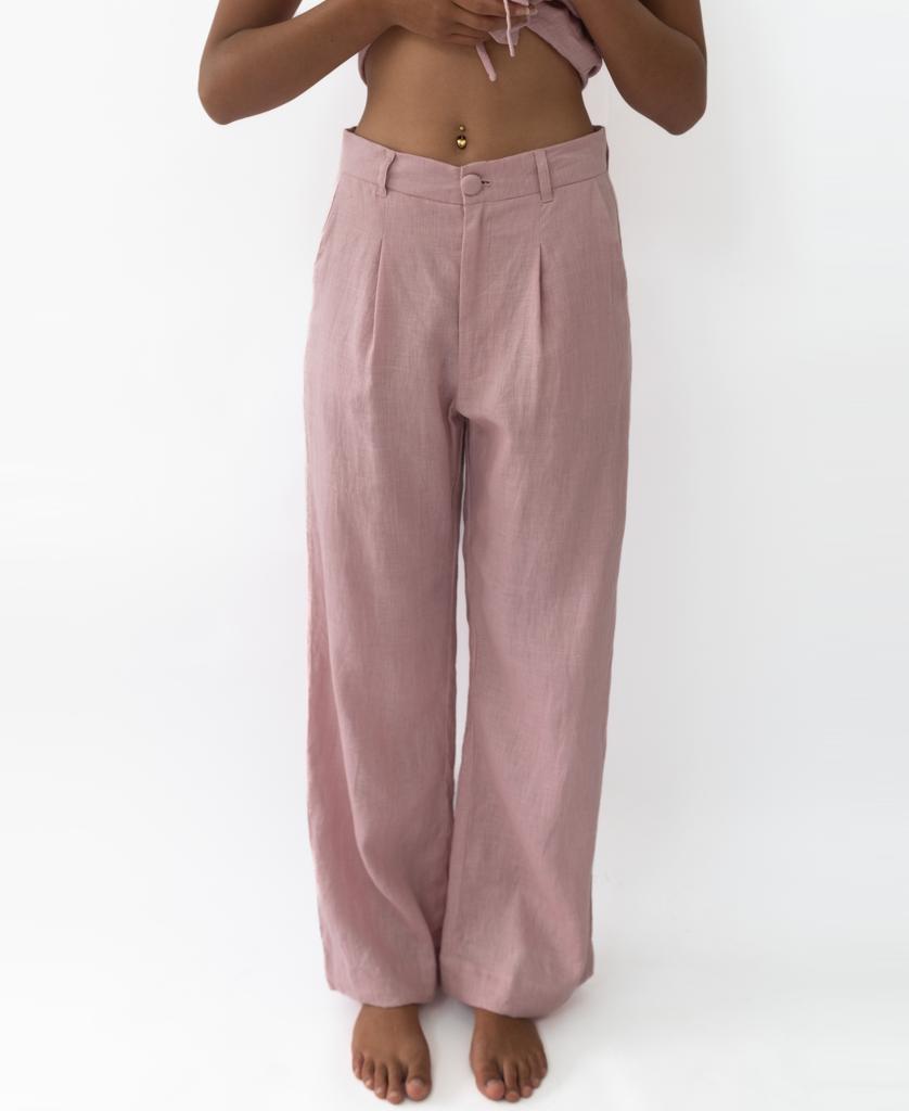 A person stands barefoot against a plain white background, wearing Lazy Beach’s Janine Pant in Linen Blush—high-waisted, oversized, structured linen—with a cropped top that shows their midriff.
