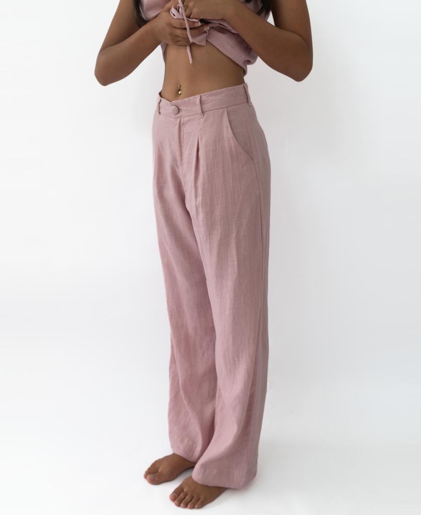 A person with long hair stands barefoot against a white background, embodying chic style in the Lazy Beach Janine Pant | Linen Blush, paired with a matching crop top for an effortlessly fashionable look.