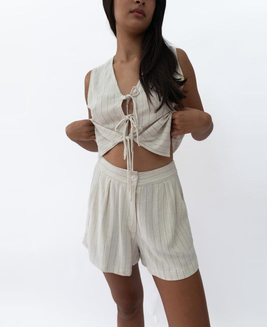 A person models Lazy Beachs Kris Short in Off White Fine Pinstripe, paired with a matching sleeveless crop top with front ties, set against a plain white background.