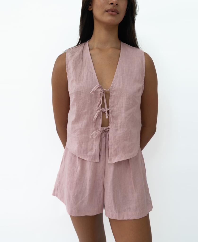 A woman wears the Lazy Beach Rennie Vest in blush linen with front ties and matching high-waisted shorts, handmade in Bali—an effortlessly stylish summer look—against a plain white background.