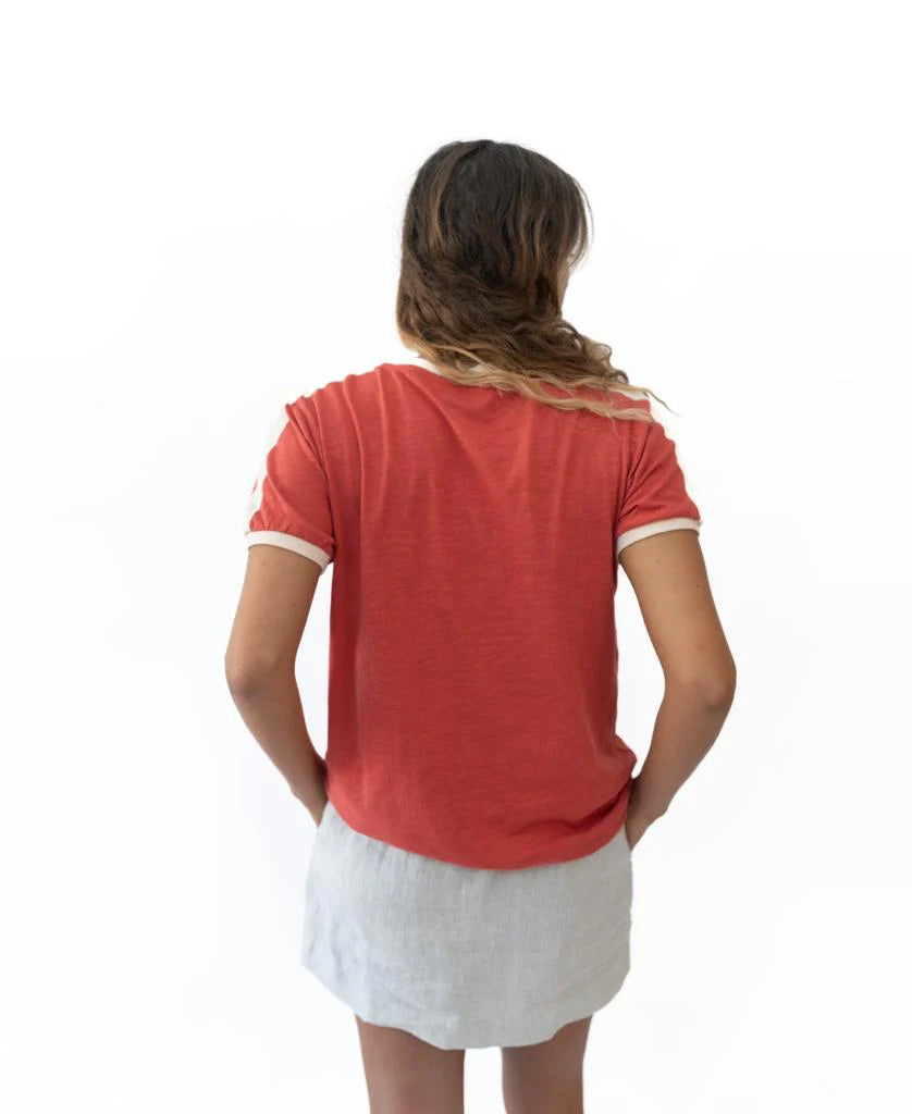 Woman wearing Retro Ringer Tee | Wash Red Beige with cream-colored sleeve cuffs and neckline, paired with a light-colored skirt, shown from the back in a casual style.