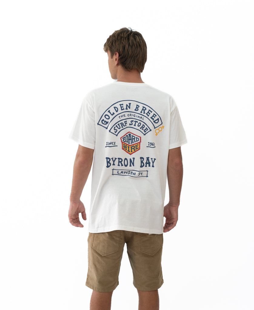 Man wearing Byron Herring Tee | Off White with retro surfwear design on the back featuring Golden Breed branding and Byron Bay text, paired with casual shorts.