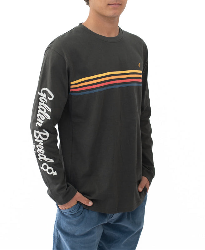 Model wearing a Heavy Island Long Sleeve Tee | Wash Black featuring retro horizontal stripes across the chest and Golden Breed branding on the sleeve, styled with casual blue pants.