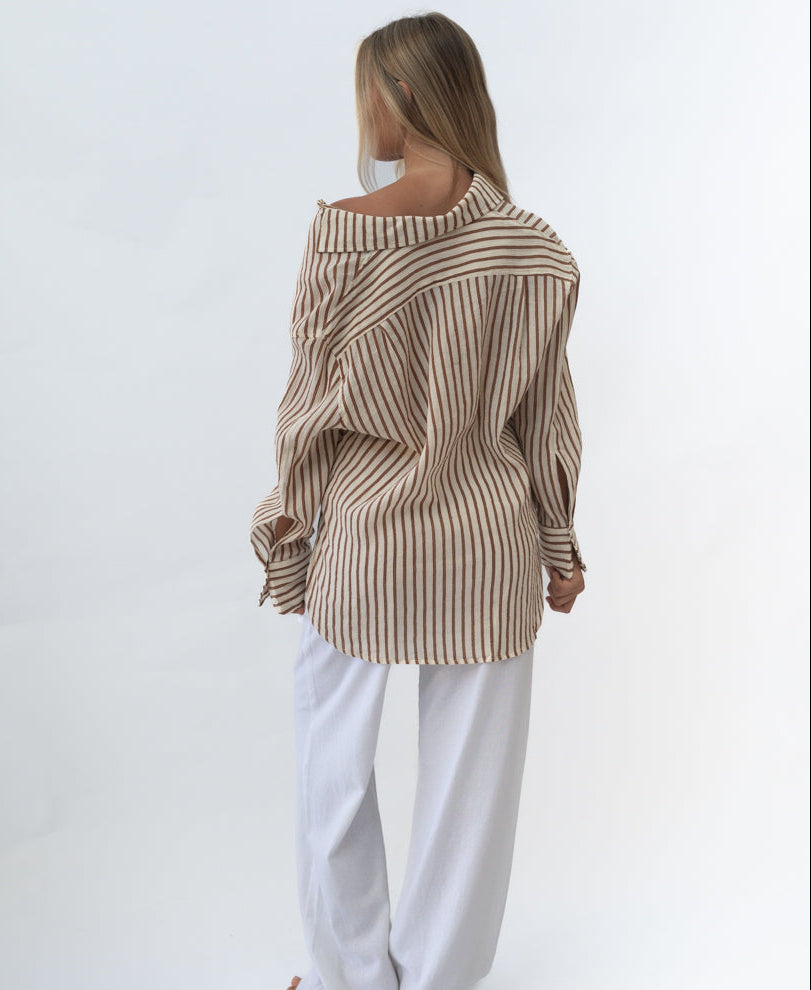 Woman wearing a loose-fitting Miley | Chestnut shirt with brown vertical stripes and white pants, shown from the back in a simple studio setting.