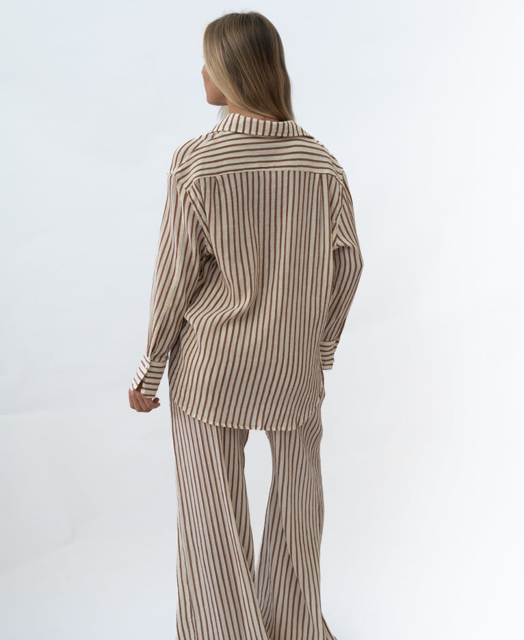 Woman wearing a relaxed fit, striped chestnut and cream shirt and matching wide-leg pants from the Miley | Chestnut collection, styled for casual Australian surfwear fashion.