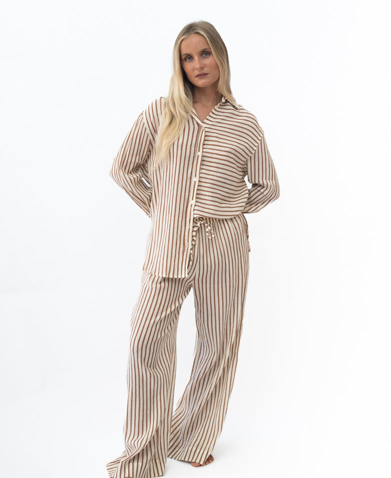 Woman wearing Miley | Chestnut relaxed striped button-up shirt and matching wide-leg pants in soft brown and cream tones, posing with hands behind back against a white background.