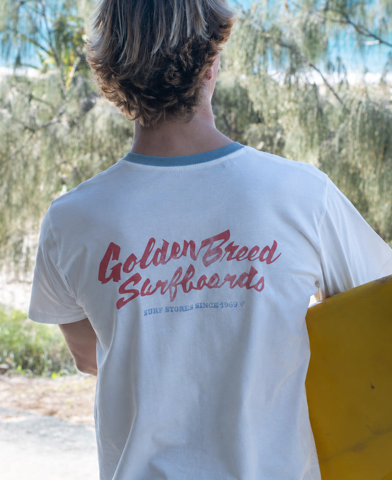 Back view of off-white surf tee with blue ringer collar, featuring red "Golden Breed Surfboards" script graphic on the back.